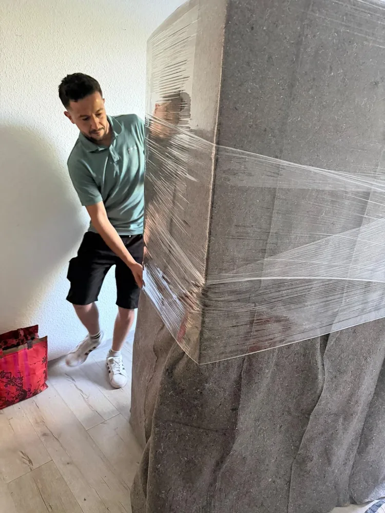 Mitarbeiter wickelt Stretchfolie um ein mit Decken geschütztes Möbelstück